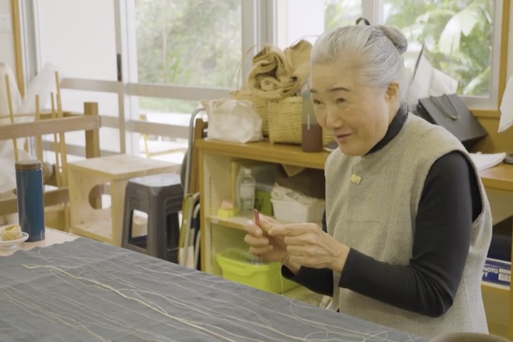 おしゃべりしながらも手は滑らかに動き、苧績み(うーうみ・取りためた繊維を裂き、一本の糸にする作業)をする、会長の津波洋子さん